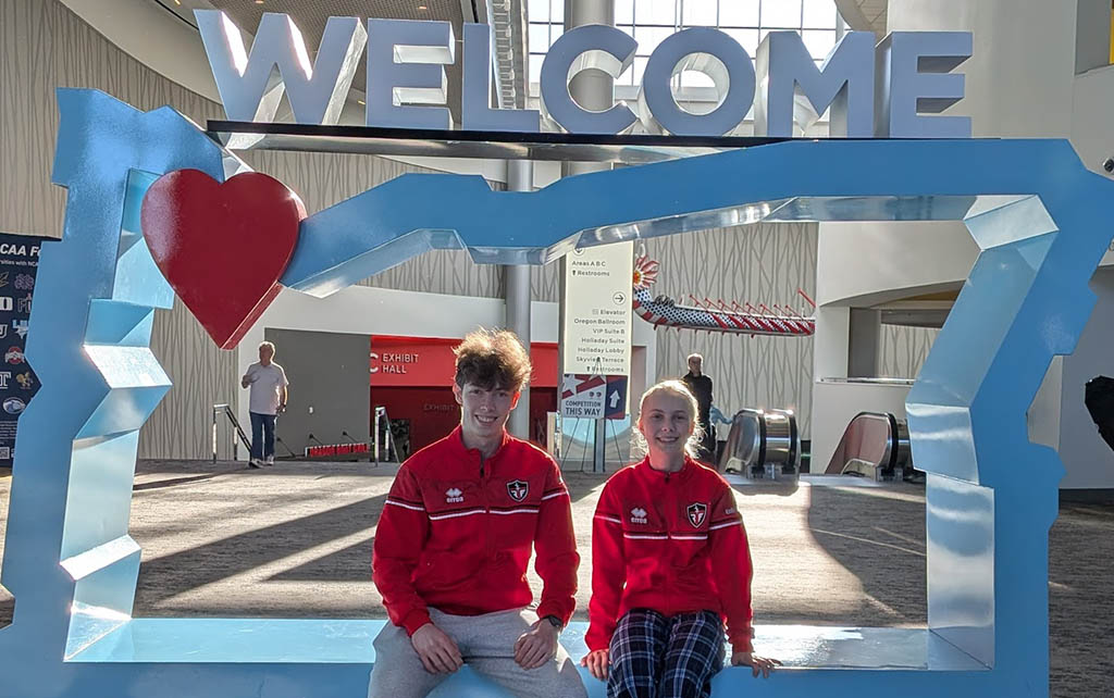 Marat and Emily sitting together in the Oregon-shaped welcome sign at the convention center